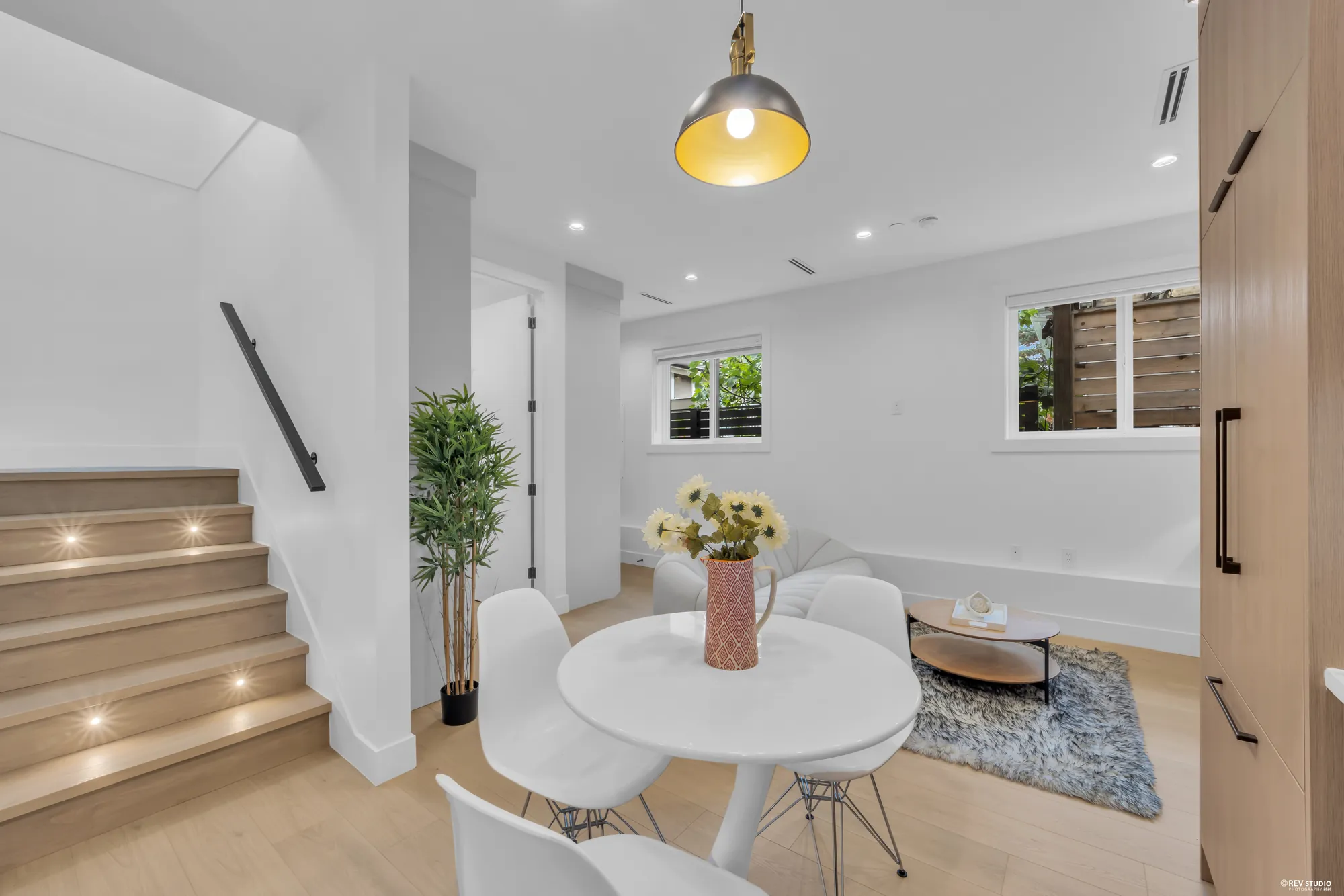 Dining table beside the stair, with a pendant light above and a plant at the foot of the stairs