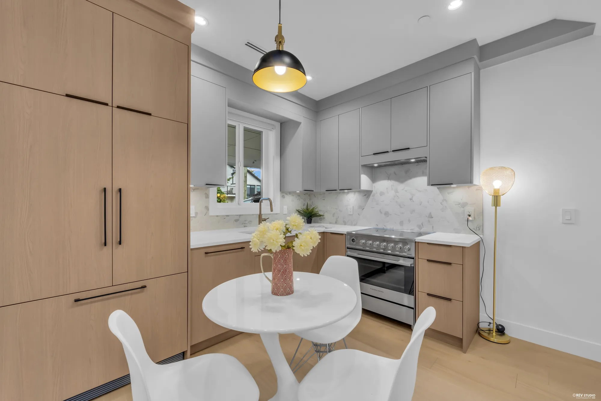 Kitchen with pale timber and white cabinets, stone counters and a range