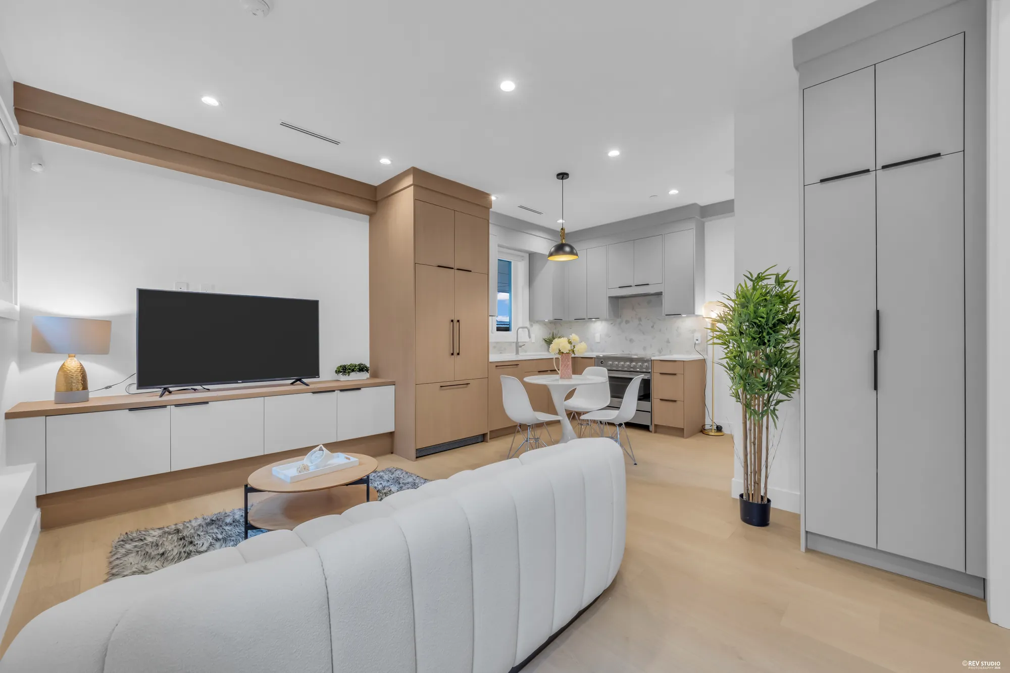 Open main floor with a curved white sofa, a television on a low cabinet and the kitchen beyond