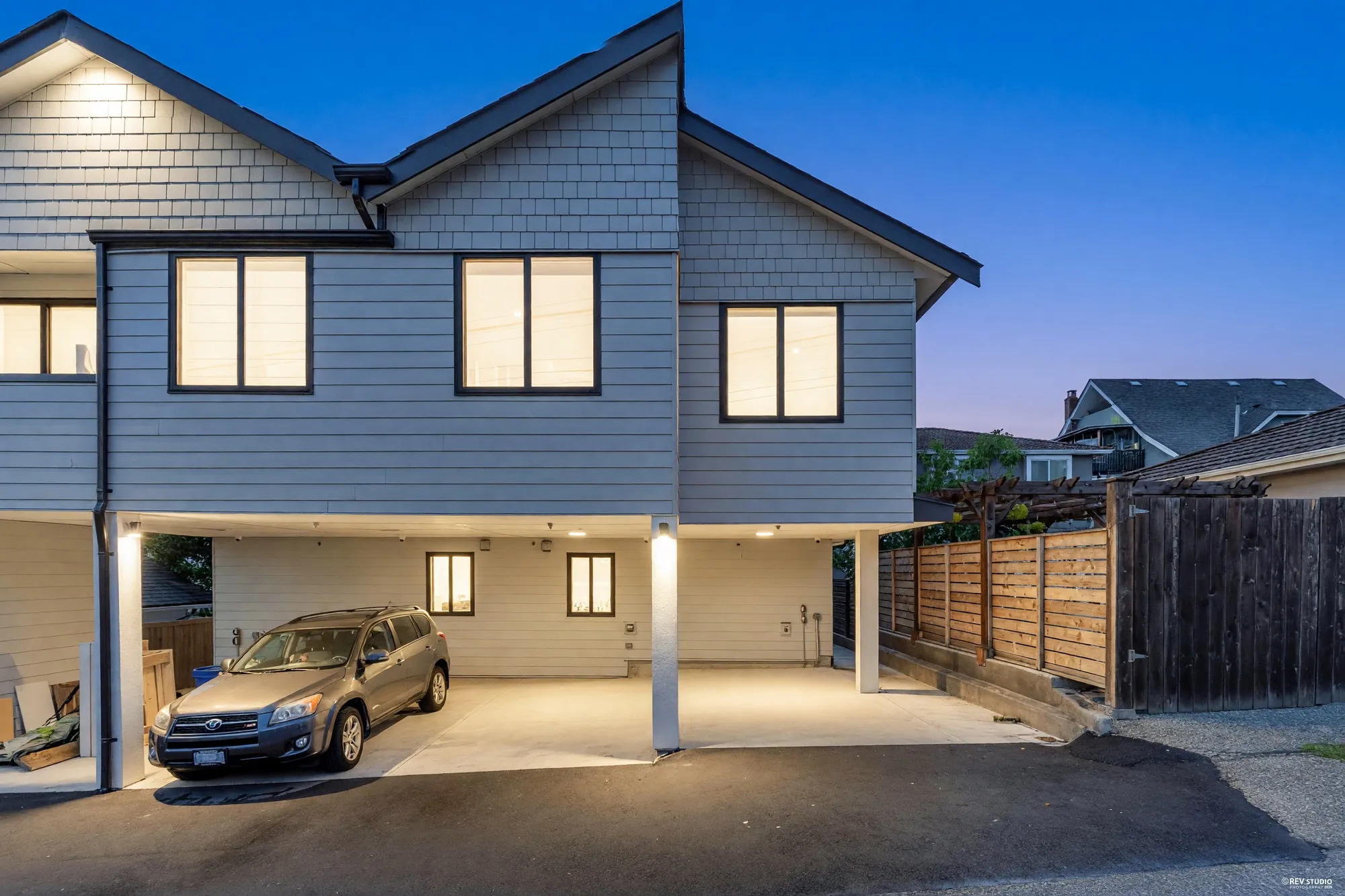 The rear building at dusk with the carport lit beneath it and a car parked underneath